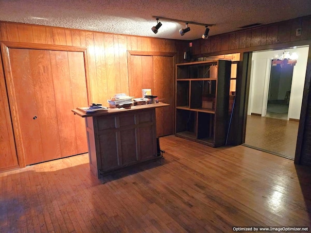 unfurnished office featuring hardwood / wood-style floors, rail lighting, wooden walls, and a textured ceiling