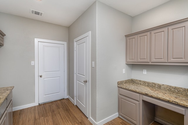 kitchen with light stone counters, hardwood / wood-style floors, and built in desk