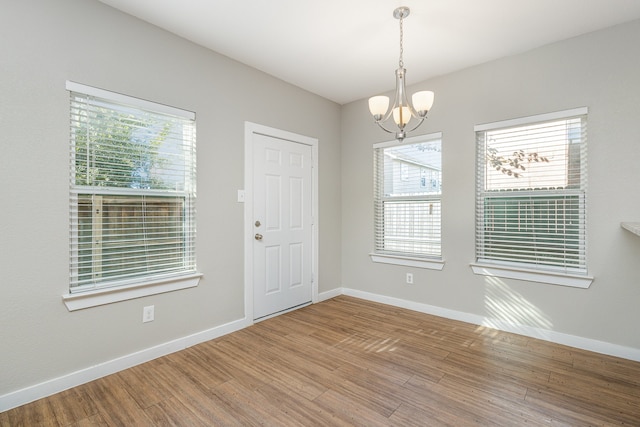 empty room with wood-type flooring, a healthy amount of sunlight, and a chandelier