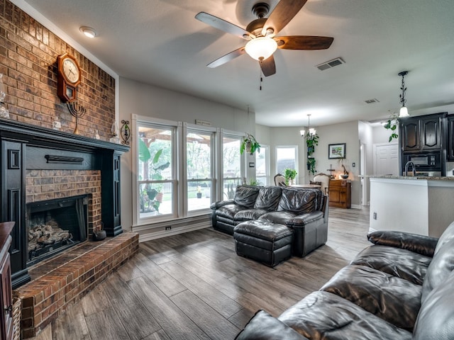 living room with a fireplace, a textured ceiling, ceiling fan with notable chandelier, and hardwood / wood-style flooring