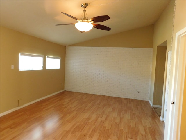 empty room featuring ceiling fan, light wood-type flooring, brick wall, and vaulted ceiling