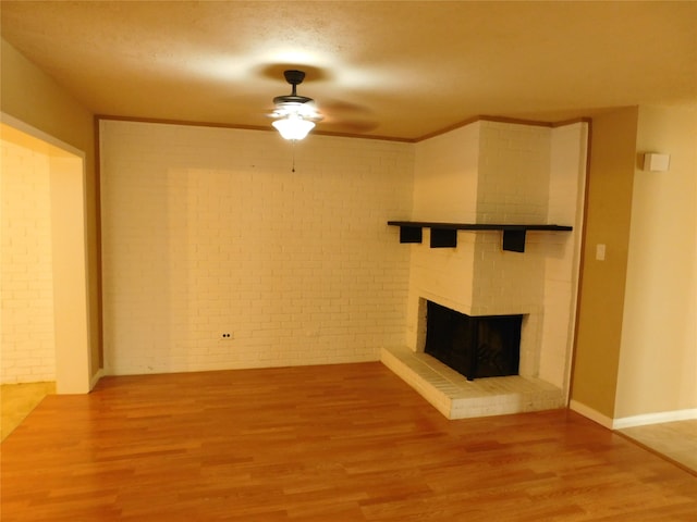 unfurnished living room featuring ceiling fan, wood-type flooring, brick wall, and a brick fireplace