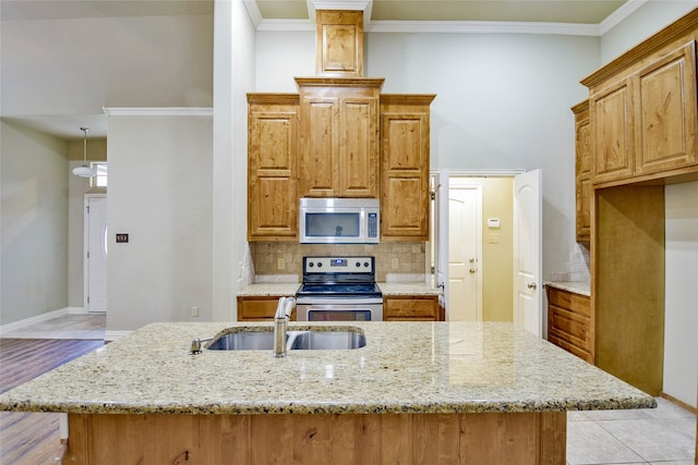 kitchen with stainless steel appliances, light stone counters, a kitchen island with sink, and sink