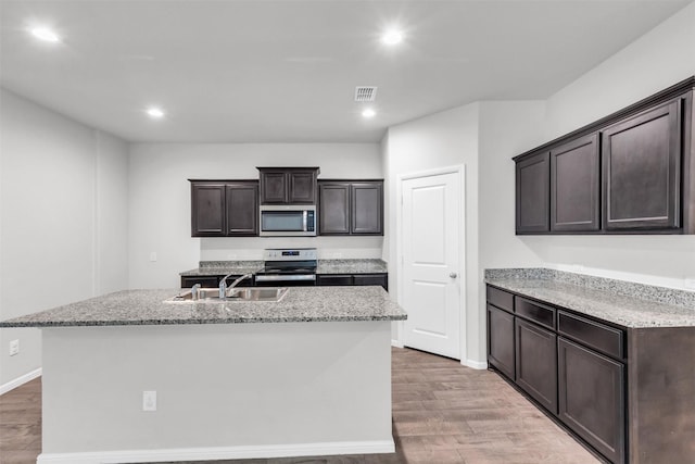 kitchen with hardwood / wood-style flooring, sink, stainless steel appliances, and a kitchen island with sink