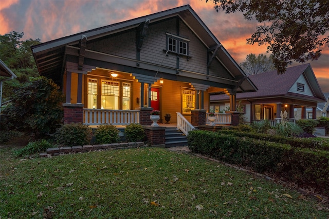 back house at dusk featuring covered porch and a lawn