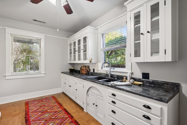 kitchen featuring dark stone counters, ceiling fan, sink, white cabinets, and light parquet flooring