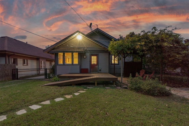 back house at dusk featuring a lawn and a wooden deck