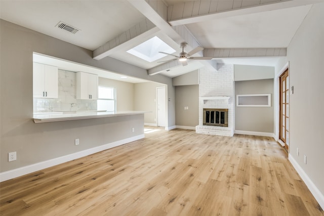 unfurnished living room with a brick fireplace, ceiling fan, vaulted ceiling with skylight, and light wood-type flooring