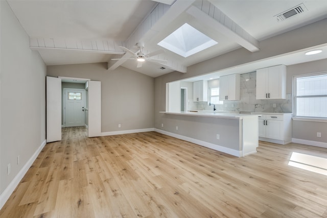 kitchen with white cabinetry, vaulted ceiling with skylight, a healthy amount of sunlight, and light hardwood / wood-style floors