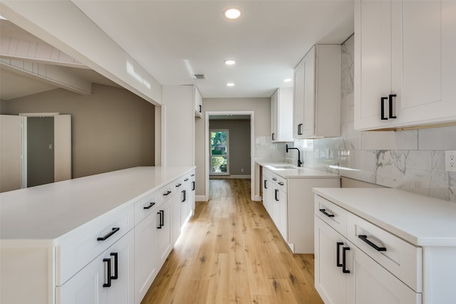 kitchen featuring white cabinetry, sink, lofted ceiling with beams, backsplash, and light hardwood / wood-style floors