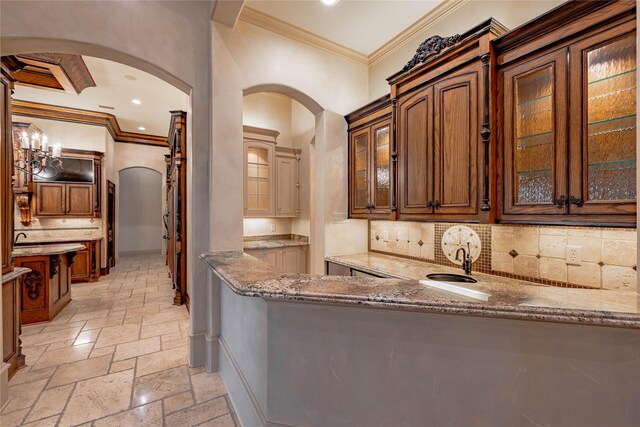 kitchen featuring an inviting chandelier, crown molding, decorative backsplash, stone countertops, and kitchen peninsula