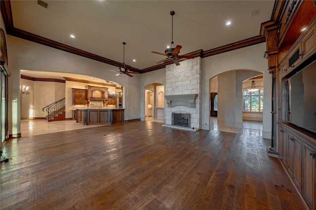 unfurnished living room featuring a stone fireplace, ceiling fan, light wood-type flooring, and ornamental molding