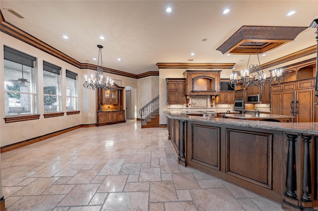 kitchen with stainless steel microwave, hanging light fixtures, crown molding, oven, and dark stone counters