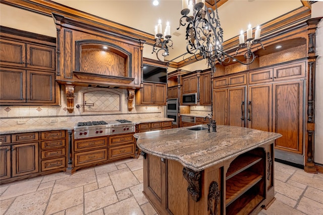 kitchen with a center island with sink, sink, built in microwave, a notable chandelier, and stainless steel gas cooktop