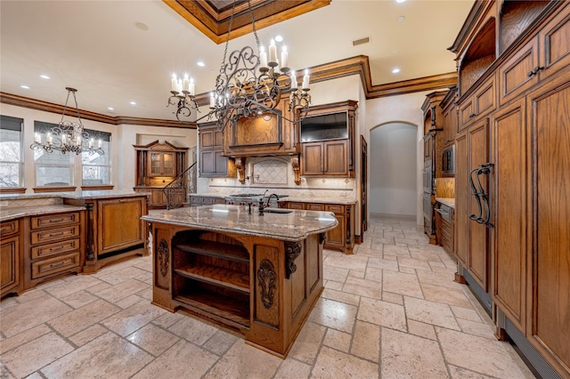 kitchen featuring sink, hanging light fixtures, decorative backsplash, ornamental molding, and an island with sink