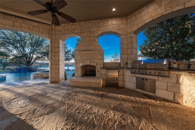 view of patio / terrace featuring a water view, an outdoor stone fireplace, ceiling fan, a grill, and exterior kitchen