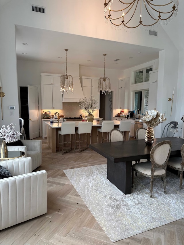 dining space featuring a high ceiling, light parquet flooring, sink, and an inviting chandelier