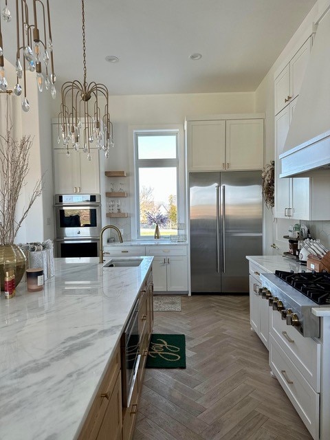 kitchen with stainless steel appliances, light stone countertops, custom range hood, white cabinets, and decorative light fixtures