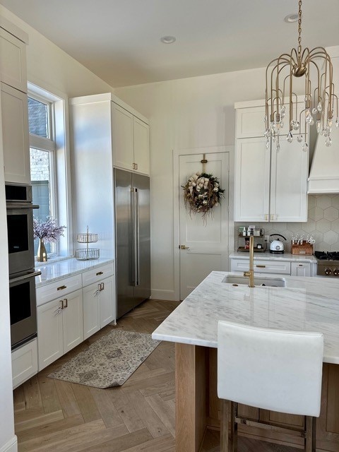 kitchen featuring light stone counters, decorative light fixtures, stainless steel appliances, and white cabinetry