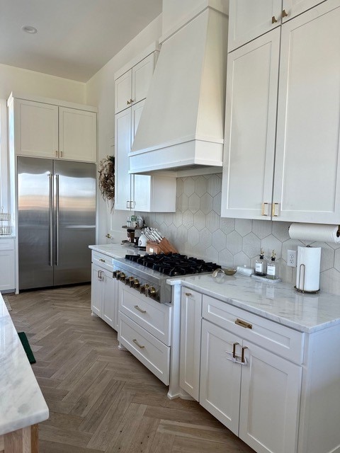 kitchen featuring premium range hood, white cabinets, stainless steel appliances, decorative backsplash, and light parquet floors