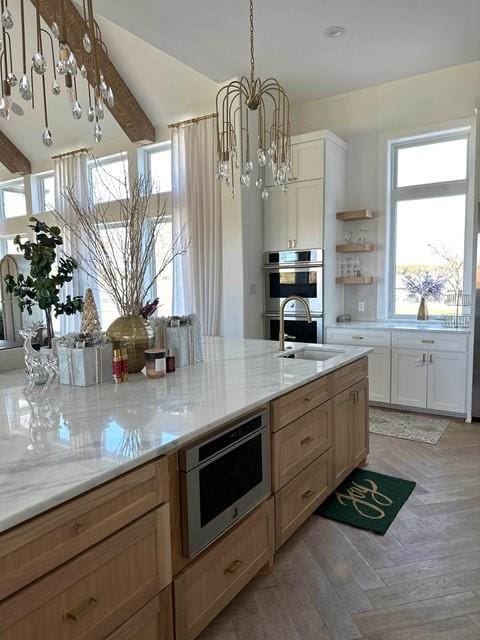 kitchen with an inviting chandelier, hanging light fixtures, double oven, light stone countertops, and white cabinets