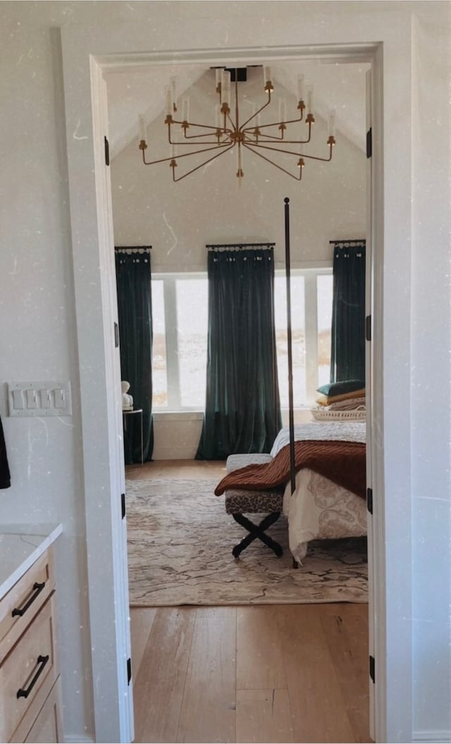 bedroom with a notable chandelier, vaulted ceiling, and light wood-type flooring