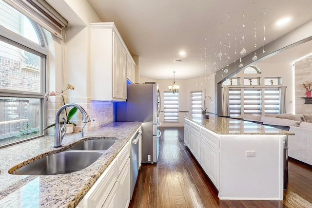 kitchen with sink, dishwasher, white cabinetry, light stone countertops, and a kitchen island