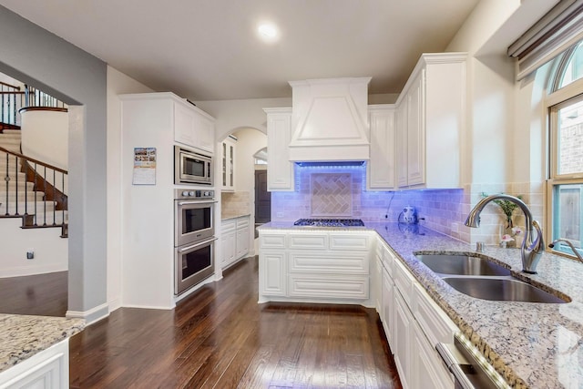 kitchen with premium range hood, dark wood-type flooring, sink, stainless steel appliances, and white cabinets