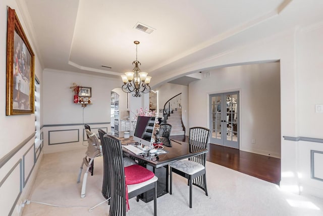 carpeted dining room featuring an inviting chandelier, a tray ceiling, crown molding, and french doors