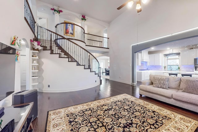 living room featuring ceiling fan, a towering ceiling, sink, and dark hardwood / wood-style flooring