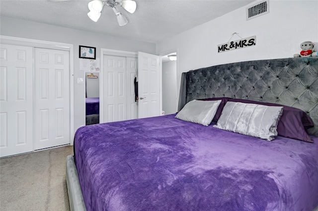 carpeted bedroom featuring multiple closets, ceiling fan, and a textured ceiling