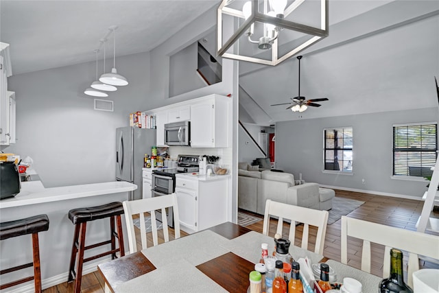 dining room featuring ceiling fan with notable chandelier, dark wood-type flooring, and high vaulted ceiling