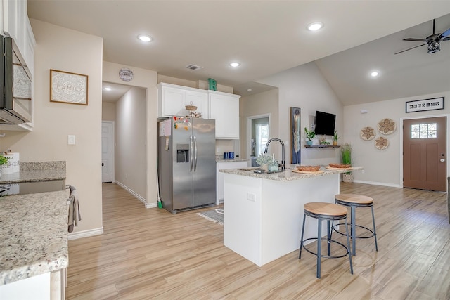 kitchen featuring light wood-type flooring, a kitchen island with sink, stainless steel appliances, white cabinets, and light stone counters