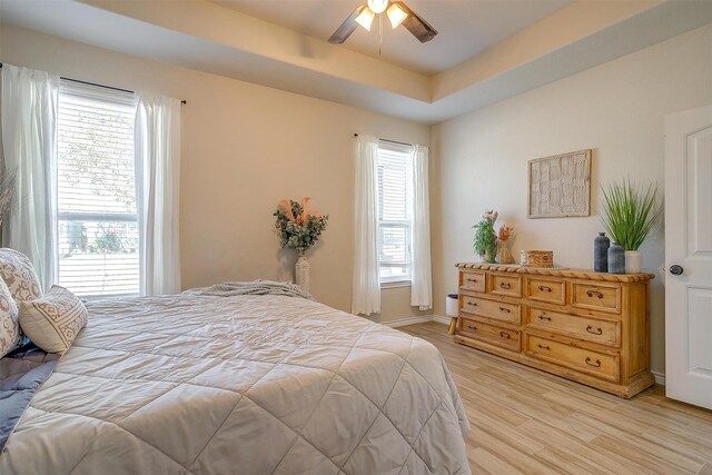 bedroom featuring a raised ceiling, ceiling fan, and light wood-type flooring