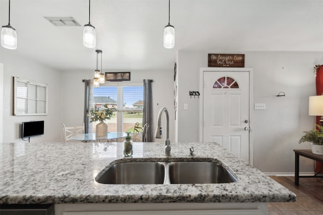 kitchen with light stone counters, decorative light fixtures, and sink