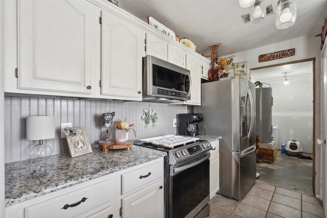 kitchen featuring light tile patterned flooring, light stone counters, a textured ceiling, appliances with stainless steel finishes, and white cabinets