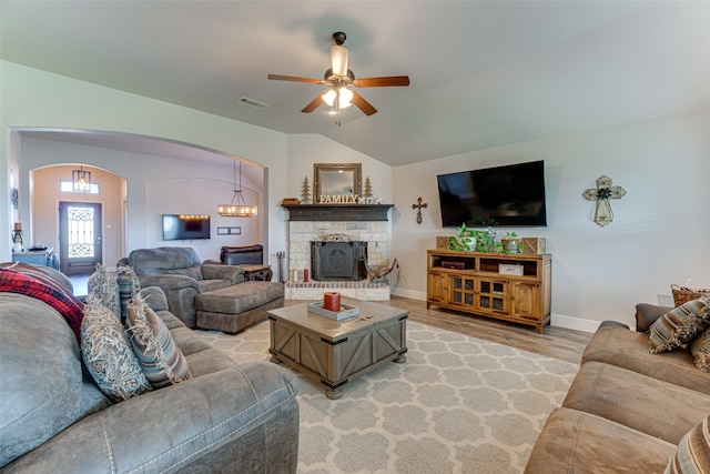 living room with ceiling fan with notable chandelier, lofted ceiling, a stone fireplace, and light hardwood / wood-style floors