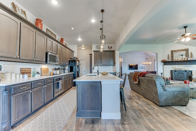 kitchen with sink, tasteful backsplash, pendant lighting, a kitchen island with sink, and black appliances