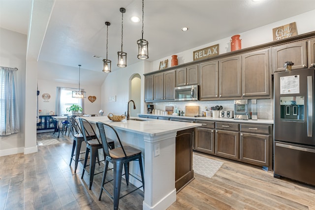 kitchen featuring pendant lighting, a kitchen bar, decorative backsplash, a kitchen island with sink, and stainless steel appliances