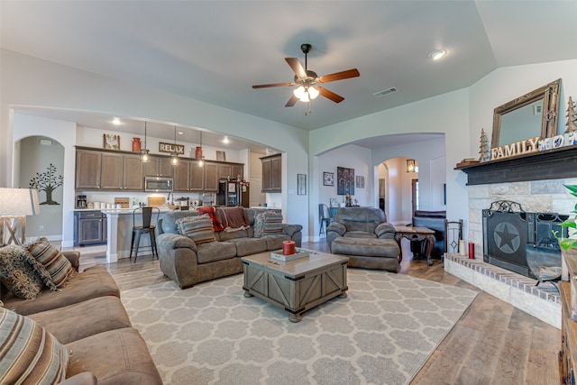 living room with vaulted ceiling, ceiling fan, a fireplace, and light hardwood / wood-style floors