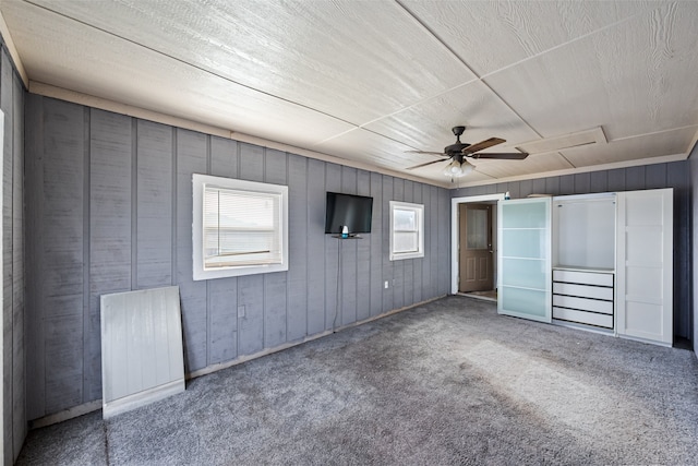 unfurnished bedroom featuring carpet, ceiling fan, and wood walls