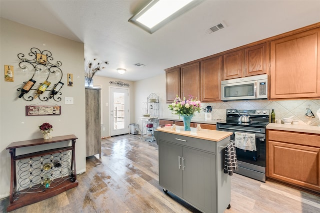 kitchen featuring light hardwood / wood-style flooring, gray cabinets, tasteful backsplash, a kitchen island, and stainless steel appliances