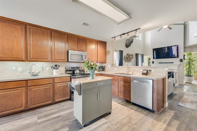 kitchen featuring sink, light wood-type flooring, appliances with stainless steel finishes, tasteful backsplash, and a kitchen island