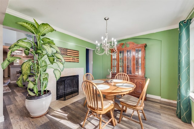 dining space with an inviting chandelier, ornamental molding, hardwood / wood-style floors, and a tile fireplace