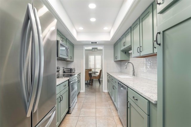 kitchen with light stone countertops, sink, green cabinets, light tile patterned flooring, and appliances with stainless steel finishes