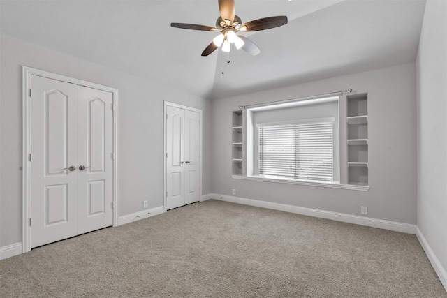 unfurnished bedroom with ceiling fan, lofted ceiling, light carpet, and two closets