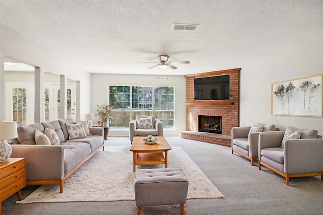 carpeted living room with ceiling fan, a fireplace, and a textured ceiling