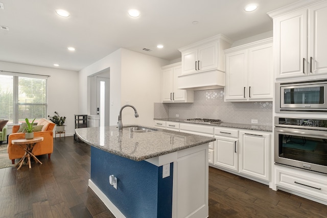 kitchen featuring sink, appliances with stainless steel finishes, light stone countertops, an island with sink, and white cabinets