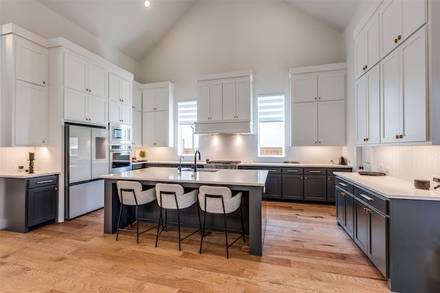 kitchen with a breakfast bar, stainless steel appliances, a kitchen island with sink, high vaulted ceiling, and light hardwood / wood-style floors