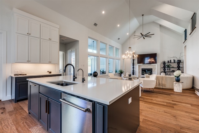 kitchen with sink, a center island with sink, high vaulted ceiling, white cabinetry, and a stone fireplace